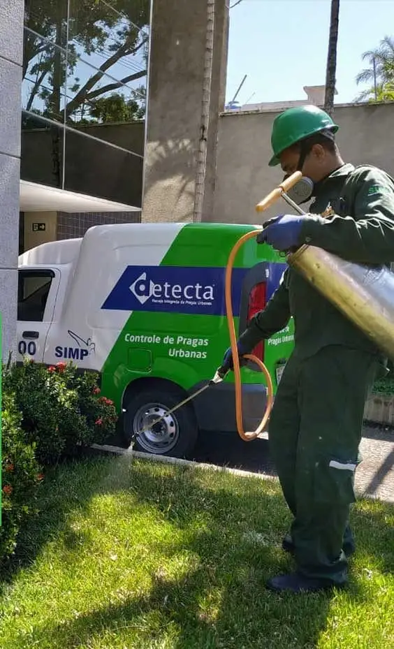 Técnico da Detecta aplicando inseticida em jardim, com o veículo da Detecta ao fundo